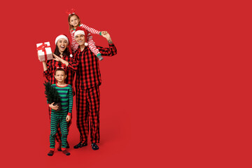 Happy family in pajamas with Christmas gift and tree on red background