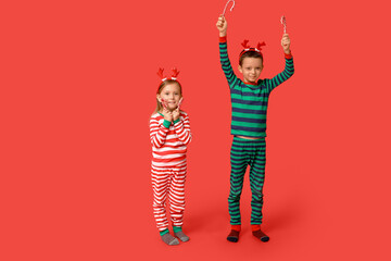 Cute little children in pajamas with candy canes on red background