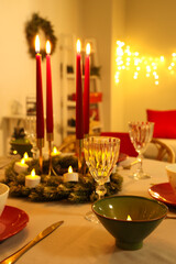 Festive table setting with burning candles and Christmas decorations in dining room at evening, closeup