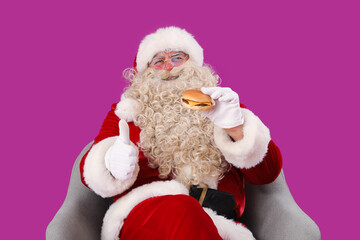 Santa Claus with tasty burger showing thumb-up on purple background