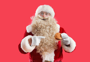 Santa Claus pointing at tasty burger on red background