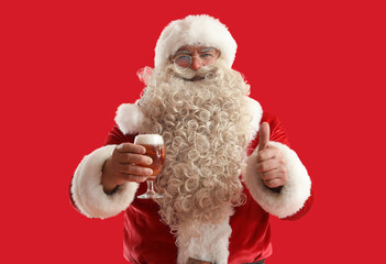 Santa Claus with glass of beer showing thumb-up on red background