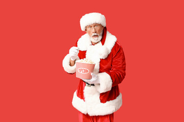 Santa Claus with bucket of tasty popcorn on red background