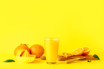 Glass of fresh orange juice and juicer on yellow background