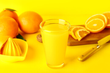 Glass of fresh orange juice and juicer on yellow background