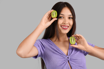 Beautiful young Asian woman with fresh kiwi on grey background