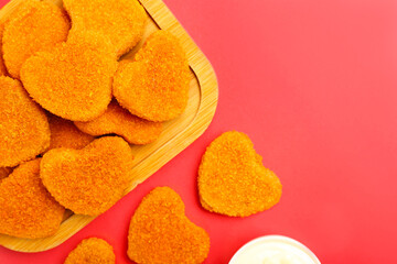 Wooden board with tasty nuggets in shape of heart on red background. Valentine's Day celebration