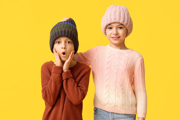 Cute little shocked children in warm winter clothes on yellow background