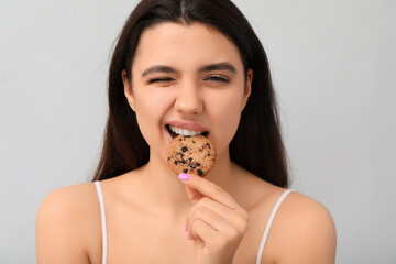 Beautiful young woman eating sweet cookie on grey background