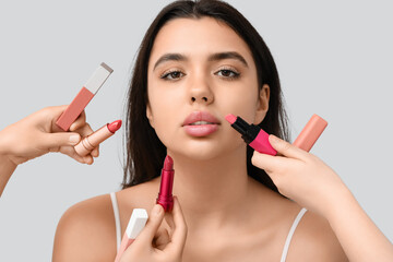 Young woman with beautiful lips and hands with different lipsticks on grey background, closeup
