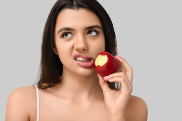 Emotional young woman with bitten apple on grey background