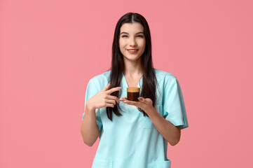 Beautiful young happy female beautician with jar of cream on pink background