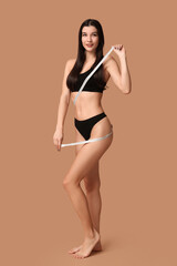 Obraz premium Beautiful young happy woman with measuring tape on brown background