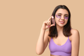 Naklejka premium Beautiful young woman with under-eye patches holding bottle of cosmetic product on color background