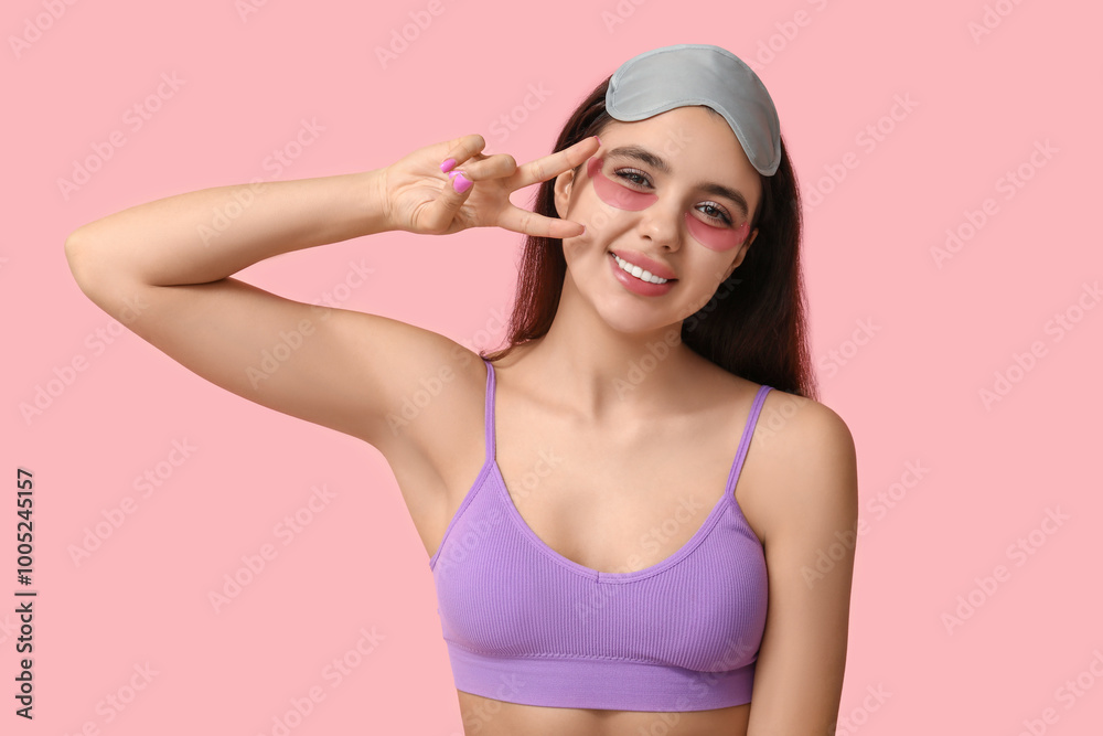 Wall mural Beautiful young woman with under-eye patches showing victory gesture on pink background