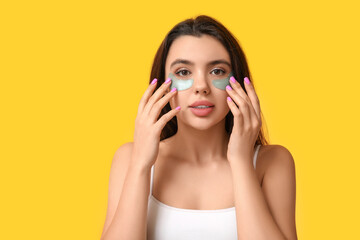 Beautiful young woman with under-eye patches on yellow background