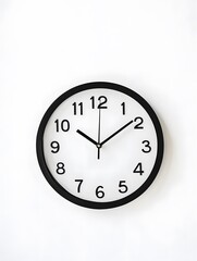 A simple black and white clock on a white wall with the time at 1200.