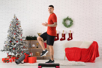 Young happy man training with aerobic stepper in living room decorated for Christmas