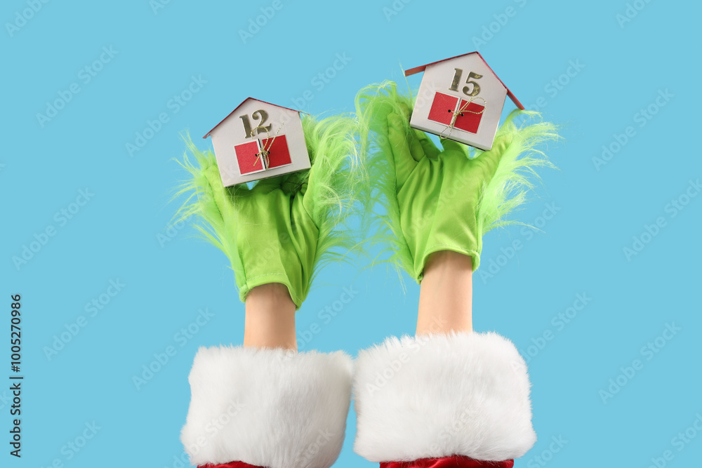 Wall mural Green hairy hands of creature in Santa costume with decorative houses on blue background