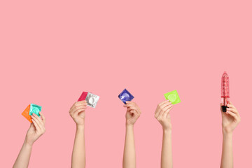 Female hands with condoms and vibrator on pink background