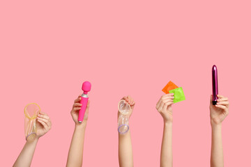 Female hands with condoms and vibrators on pink background