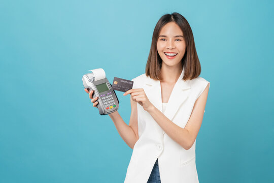 Cheerful beautiful Asian women holding credit card for payment on card reader machine, isolated on blue background.