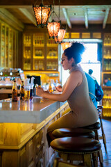 Young Latina woman smiling at a bar counter, enjoying a drink in a well-lit bar setting at Museo Larco in Lima, Peru.
