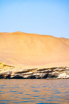 The famous Candelabra geoglyph etched into the sand dunes at Paracas Peninsula, Peru, under a clear blue sky.