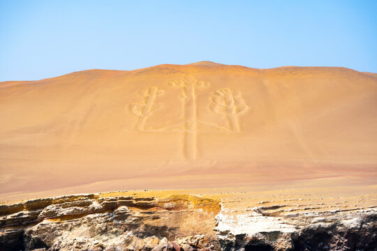 The famous Candelabra geoglyph etched into the sand dunes at Paracas Peninsula, Peru, under a clear blue sky.