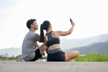 A lovely, sporty Asian couple is taking a selfie together while resting after their morning run.