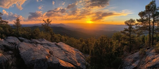 Naklejka premium Sunset over a mountain range with trees and rocks in the foreground.