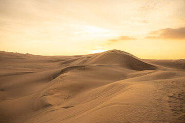 Breathtaking golden sunset over the sand dunes in Huacachina, Ica, Peru, creating a serene desert landscape. © Itza