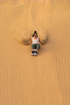 Young woman enjoying an exciting sandboarding experience down the sand dunes in Huacachina, Ica, Peru, creating a thrilling adventure.