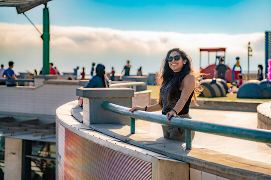 Young Latina woman smiling and enjoying the ocean view on a sunny day in Larcomar, Miraflores, Lima, Peru, with the coastline and mountains in the background.