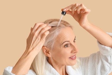 Fototapeta premium Mature woman applying cosmetic oil on hair against color background, closeup