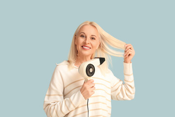 Fototapeta premium Mature woman with hair dryer on color background