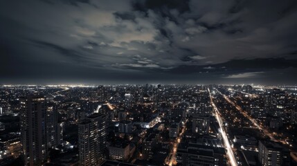 A panoramic night view of a city with buildings, streets and a cloudy sky.