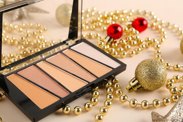 Beautiful composition with Christmas balls, eyeshadow palette and shiny golden beads on beige background, closeup
