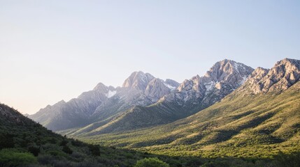 Fototapeta premium photo of the majestic beauty of a towering mountain range, with rugged peaks covered in snow, lush green valleys below, and a clear blue sky, creating a breathtaking natural landscape