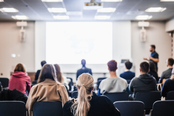 Fototapeta premium Speaker giving a talk in conference hall at business event. Rear view of unrecognizable people in audience at the conference hall. Business and entrepreneurship concept