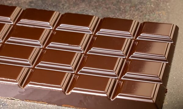 Mouvements de cam&eacute;ra sur la surface d'une tablette de chocolat au lait, texture lisse, brillante et app&eacute;tissante du chocolat au beurre de cacao
