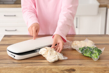Young woman with vacuum sealer machine for food and vegetables in packs on kitchen table