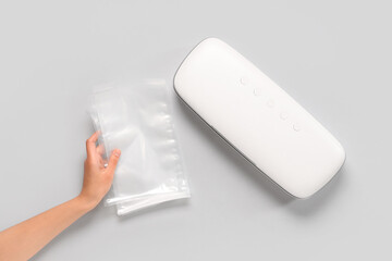 Female hands with packs and vacuum sealer machine for food on white background