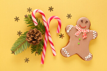 Christmas composition with tasty gingerbread man, candy canes and fir tree branches on beige background