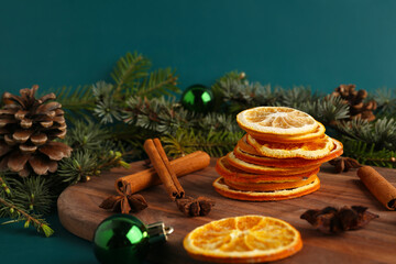 Wooden board with dried orange slices, spices and Christmas decorations on color background
