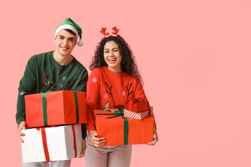 Happy young couple in Christmas sweaters with gift boxes on pink background