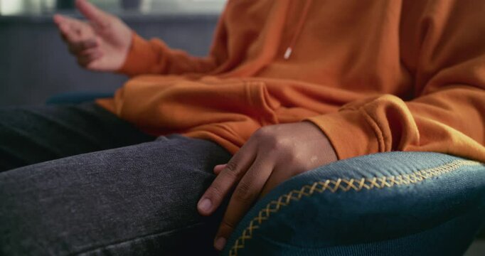 Close up of African American teenage boy sitting in chair, gesturing during communication with psychologist or therapist. Therapy session and psychological support for teenagers. Psychology concept.