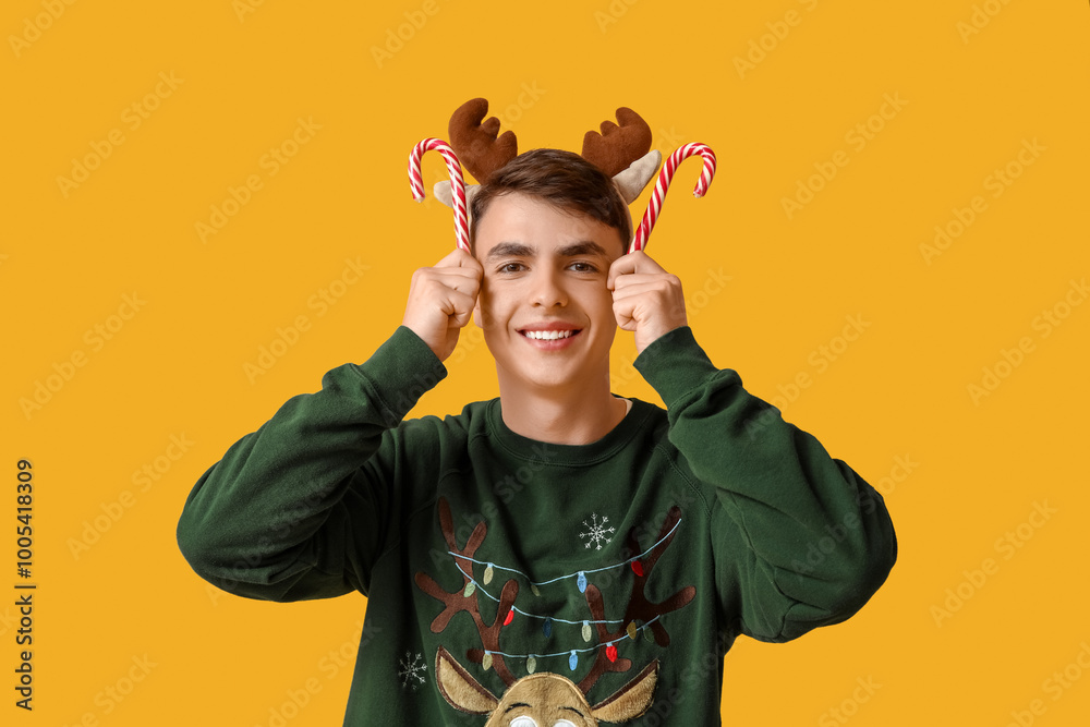 Sticker Happy young man in Christmas sweater and deer horns with candy canes on yellow background