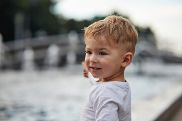 Close-up of a thoughtful young boy with light brown hair and blue eyes, looking off into the distance. The child is wearing a white t-shirt. Perfect for concepts of curiosity, childhood, innocence.