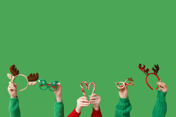 Female hands holding candy canes and festive accessories on green background